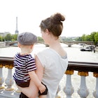 A mom and baby in France, standing on a bridge overlooking the Eiffel Tower.
