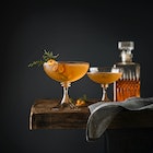 Two whiskey cocktails with citrus peels in coupe glasses set on bar 