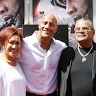Dwayne Johnson is on a red carpet with his mother to his left and his late dad, Rocky Johnson, to hi...