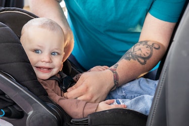 Happy baby is smiling while being buckled into car seat in family car