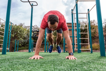 A man doing burpees outside on a playground.