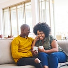 Husband and wife sitting on the couch with coffee, having a happy conversation and laughing