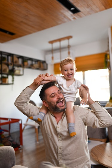 Smiling Baby Boy Enjoying Ride On Father's Shoulders At Home