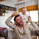 Smiling Baby Boy Enjoying Ride On Father's Shoulders At Home
