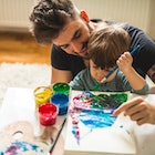 A dad helping his child paint artwork.