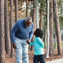 An African-American boy and his grandfather walking together in a park, holding hands, looking at ea...